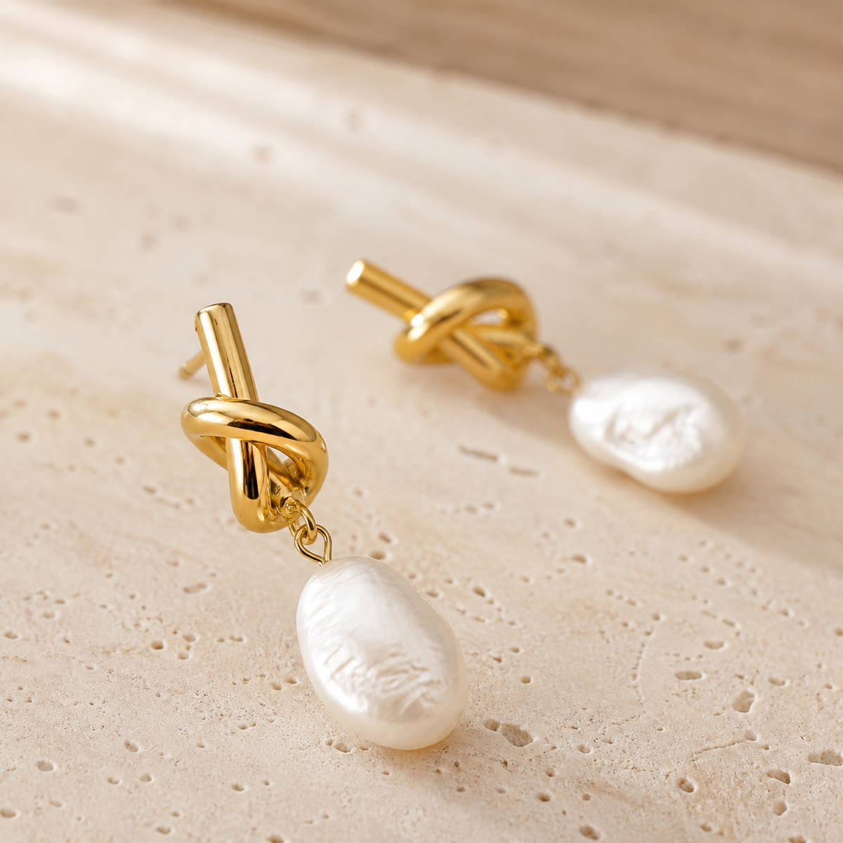 Macro detail of gold sculptural knot and white baroque pearl drop earrings