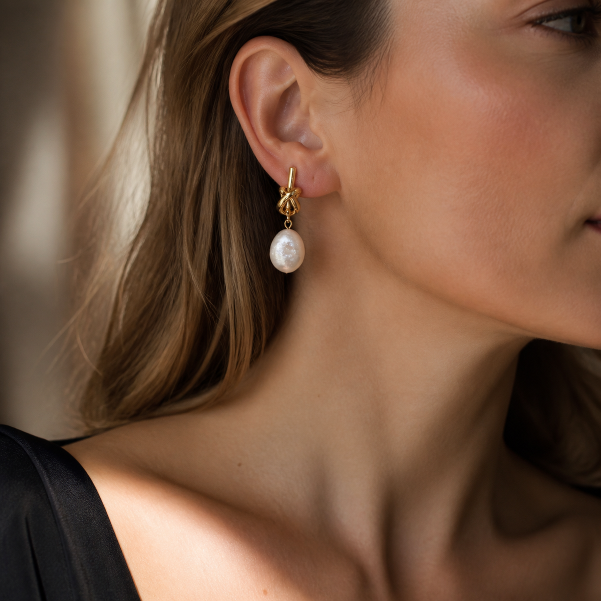 Woman wearing gold knot earrings with white baroque pearl drops